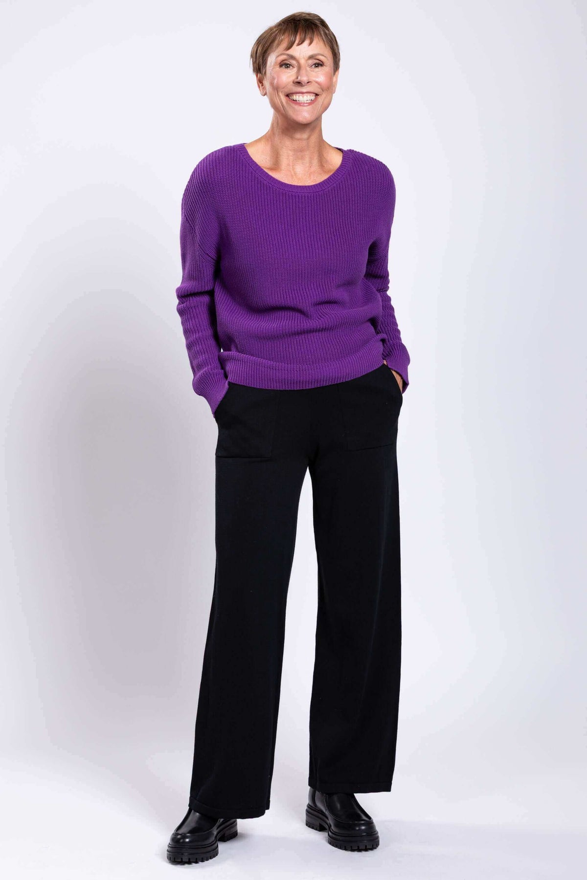 Full-body view of woman smiling in purple cotton sweater and black pants