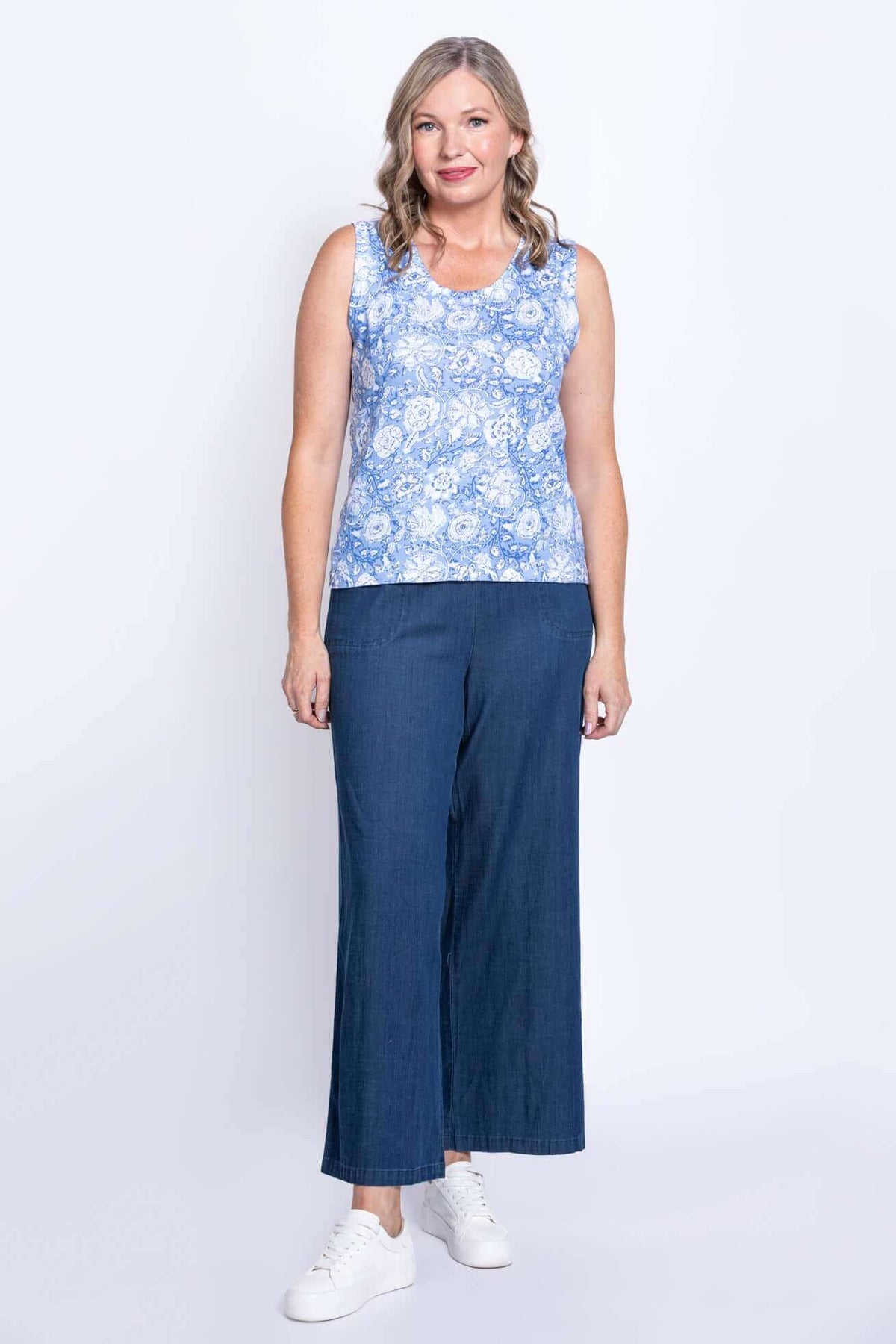Full-body view of a woman in a blue floral tank top and wide-leg jeans