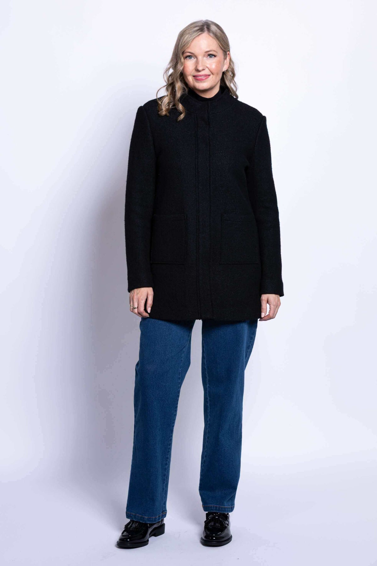 Full-length front view of woman in black boiled wool coat and blue jeans