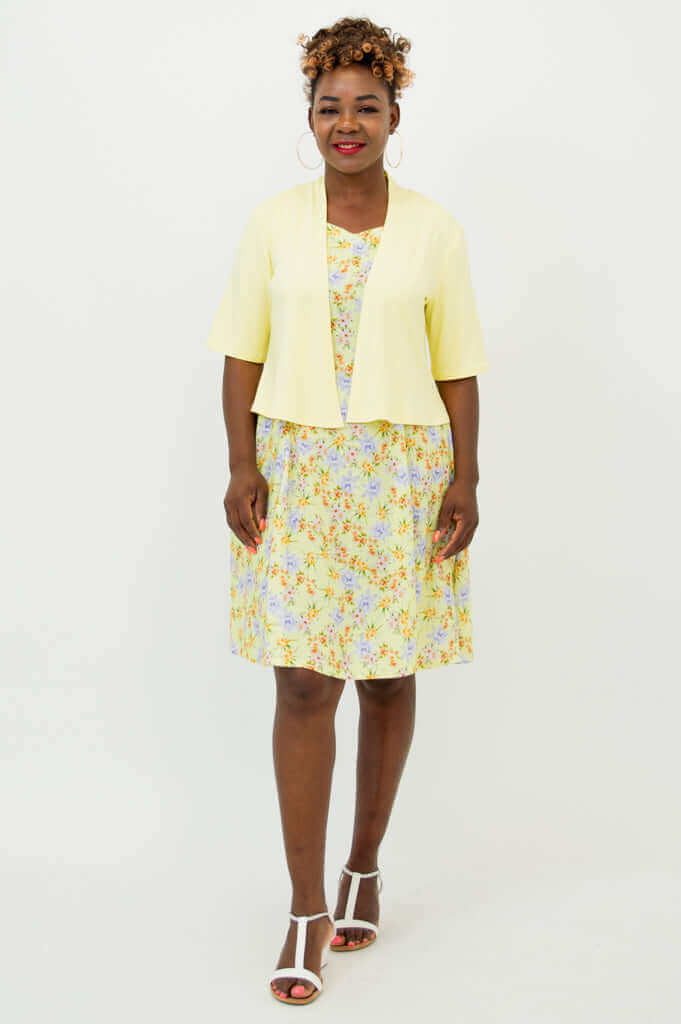 Front view of woman in cropped yellow jacket and floral dress with white sandals