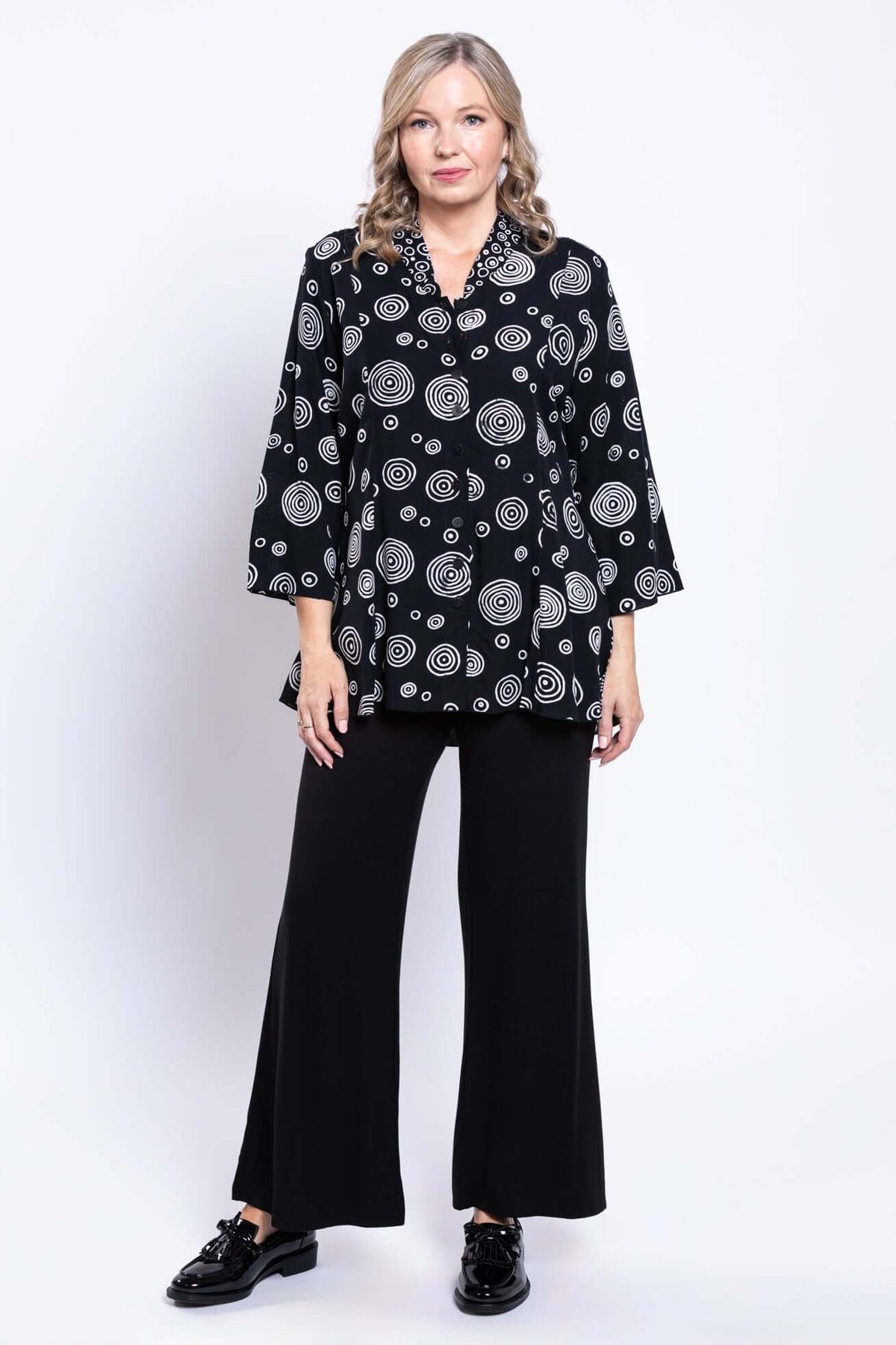 Full-length front view of a woman in a black and white circle print blouse with black pants