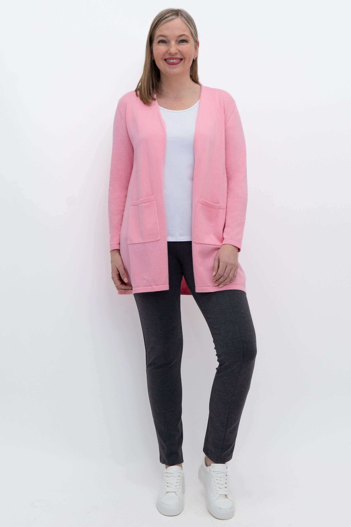 Full-length front view of a woman modeling a pink open cardigan over a white top and gray pants