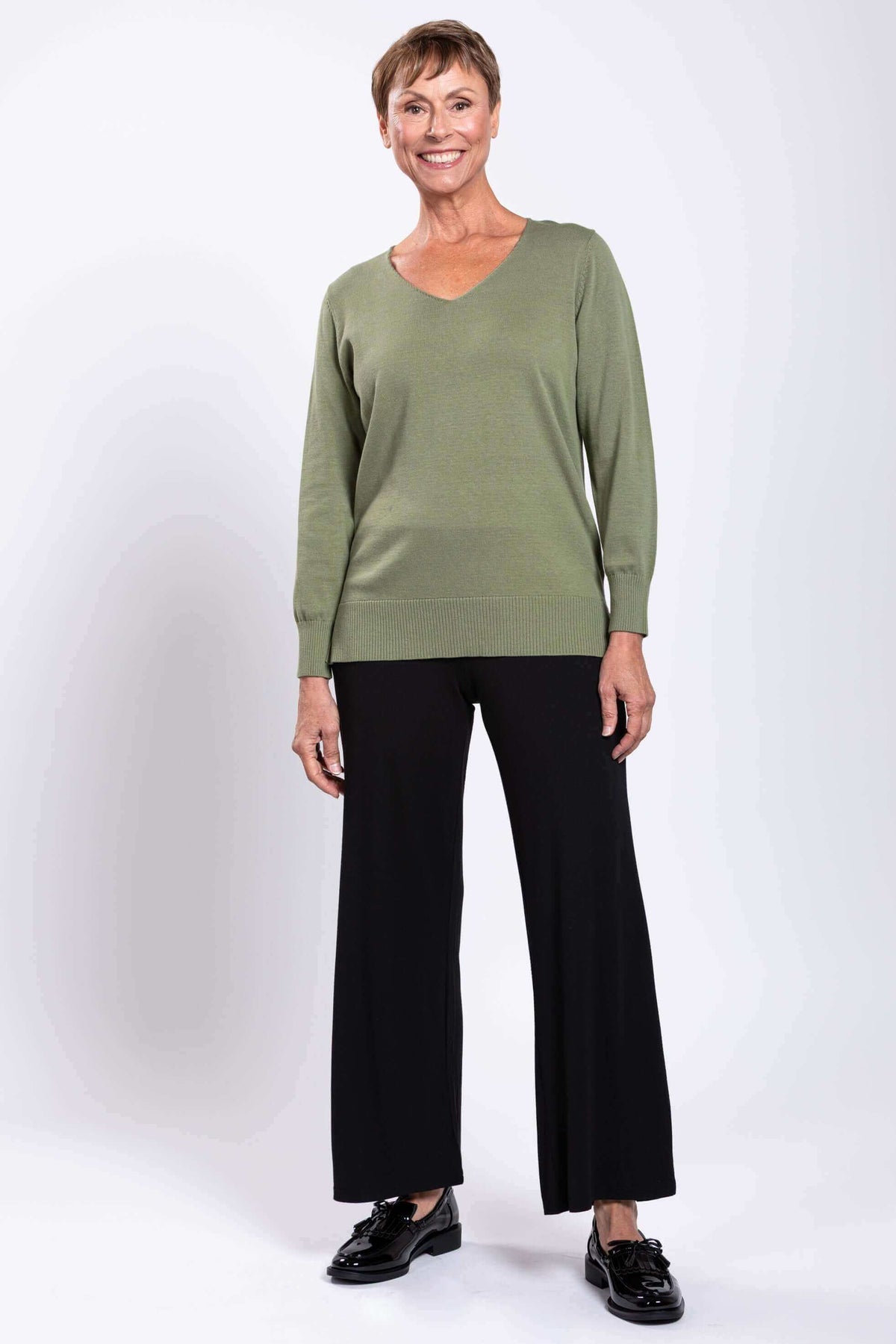 Full-length front view of a woman in a green V-neck sweater with black pants and shoes