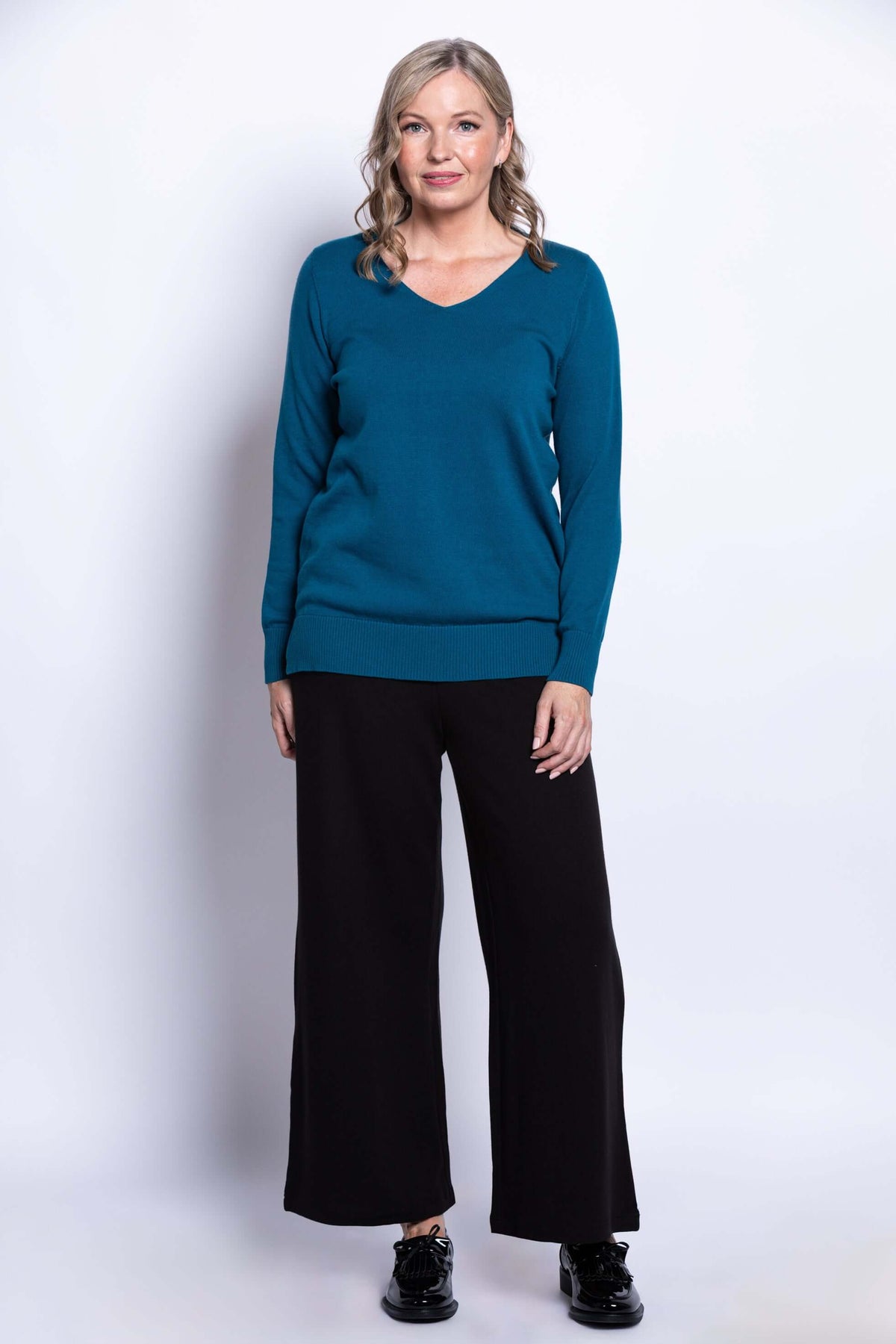 Full-length front view of woman in teal V-neck sweater paired with black pants