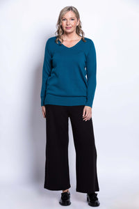 Full-length front view of woman in teal V-neck sweater paired with black pants