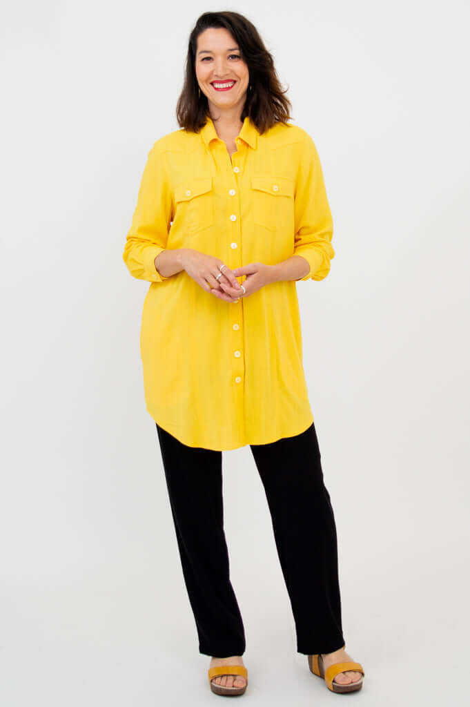 Full-length view of woman in a yellow button-up shirt tunic with black pants and sandals