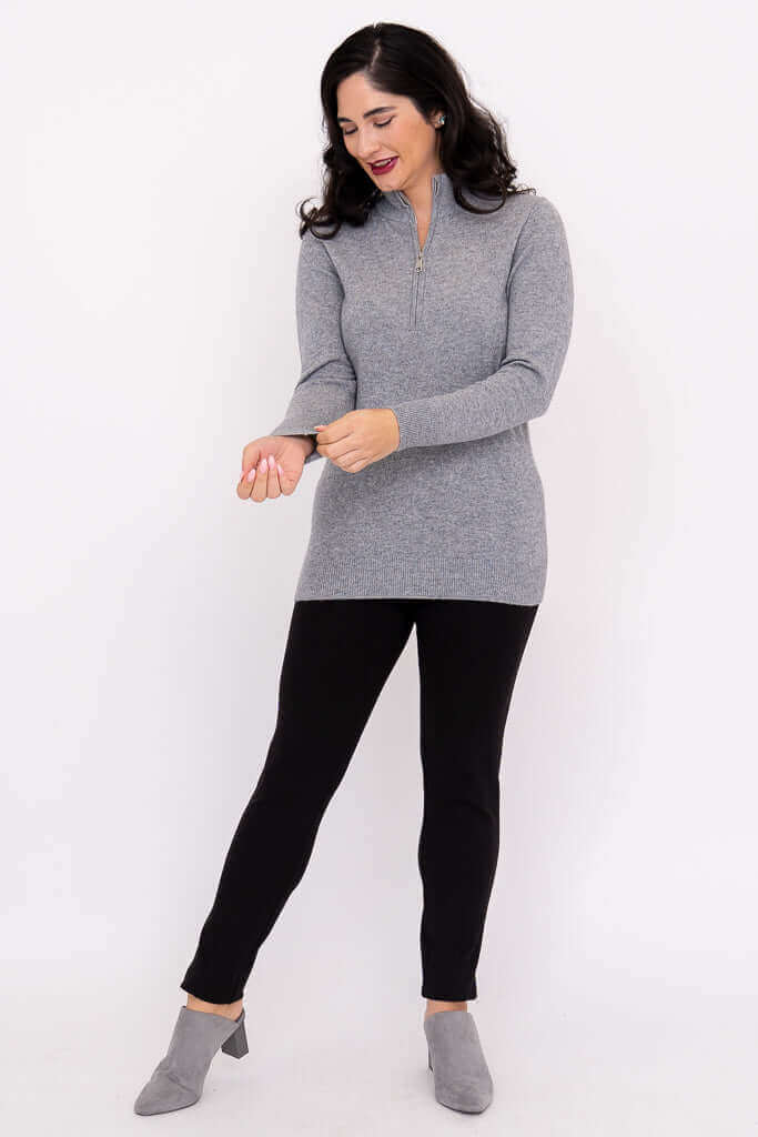 Woman adjusting her sleeve in a full-length view of grey half zip sweater and black pants