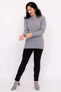 Woman adjusting her sleeve in a full-length view of grey half zip sweater and black pants