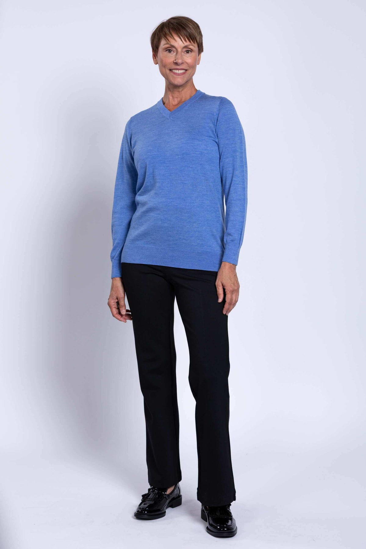 Woman standing in blue Merino V-neck sweater, full-length view
