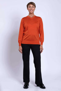 Full-length view of woman in tangerine V-neck merino sweater and black pants.