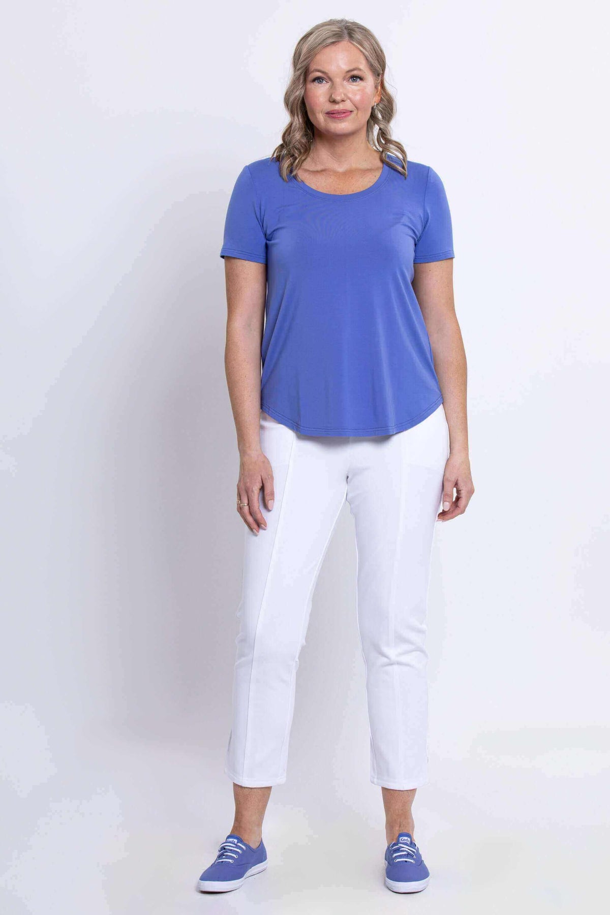 Full body view of woman in an azure blue bamboo tee and white pants, facing forward