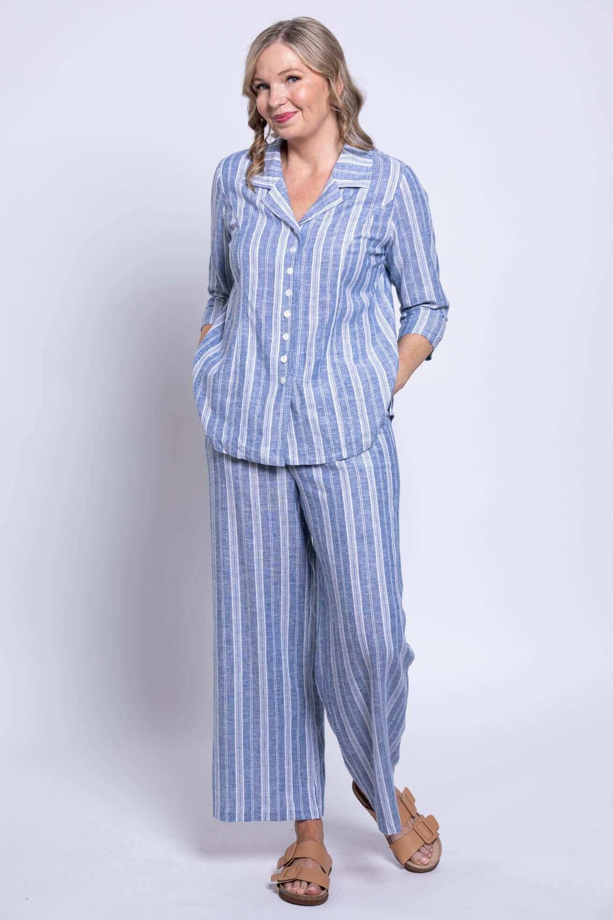 Full outfit view of model in blue striped button-up blouse and matching pants, hands in pockets