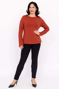 Full body view of model in rust Mona boat neck top and black pants, hand on hip