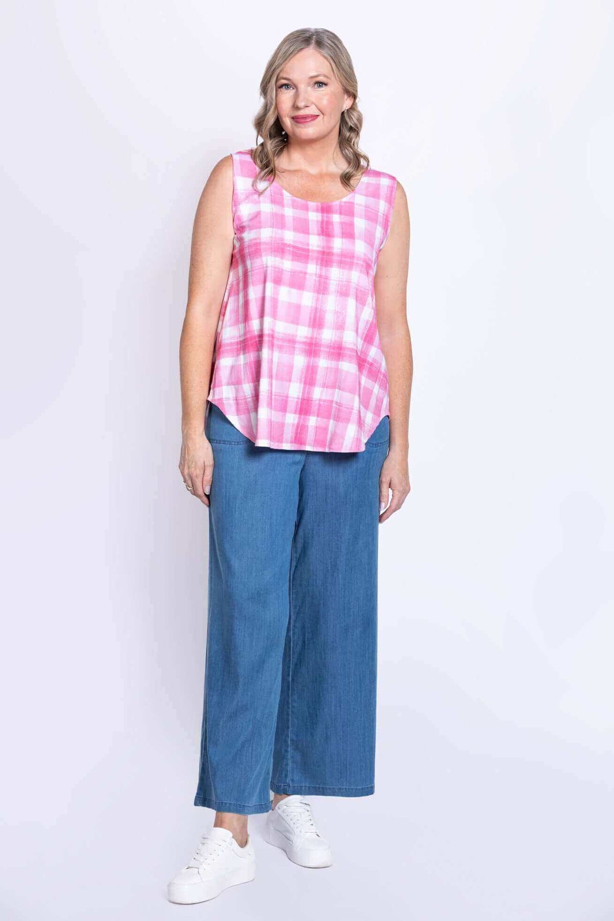 Full body angled view of woman in pink plaid tank top, jeans, and white sneakers