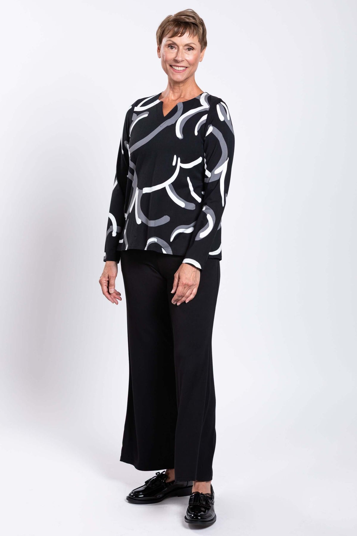 Full body angled view of model smiling in swirl print top and black pants