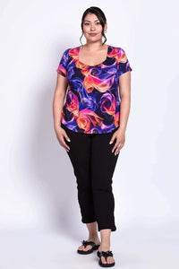Full body front view of model in neon swirl patterned top, black pants, and black sandals