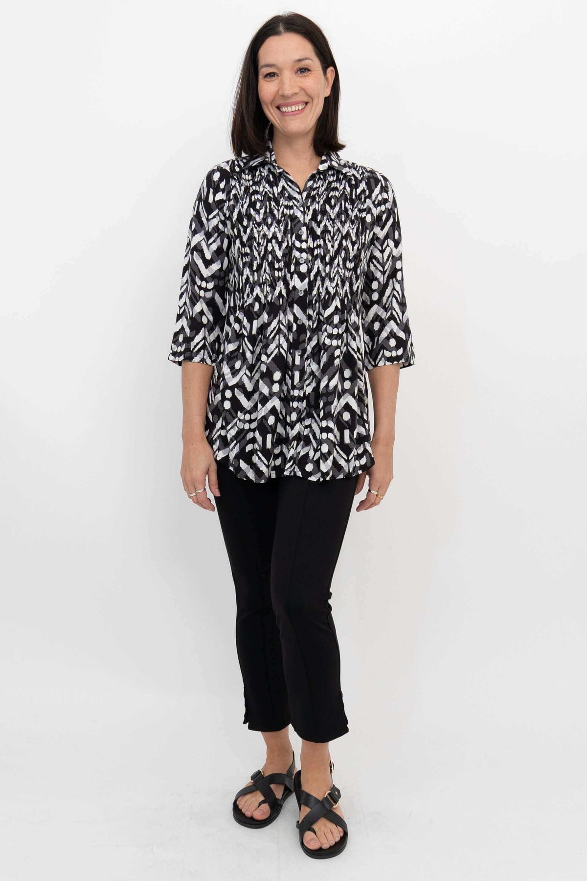 Full body front view of a woman modeling a black and white Ikat smocked blouse and black pants