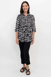 Full body front view of a woman modeling a black and white Ikat smocked blouse and black pants