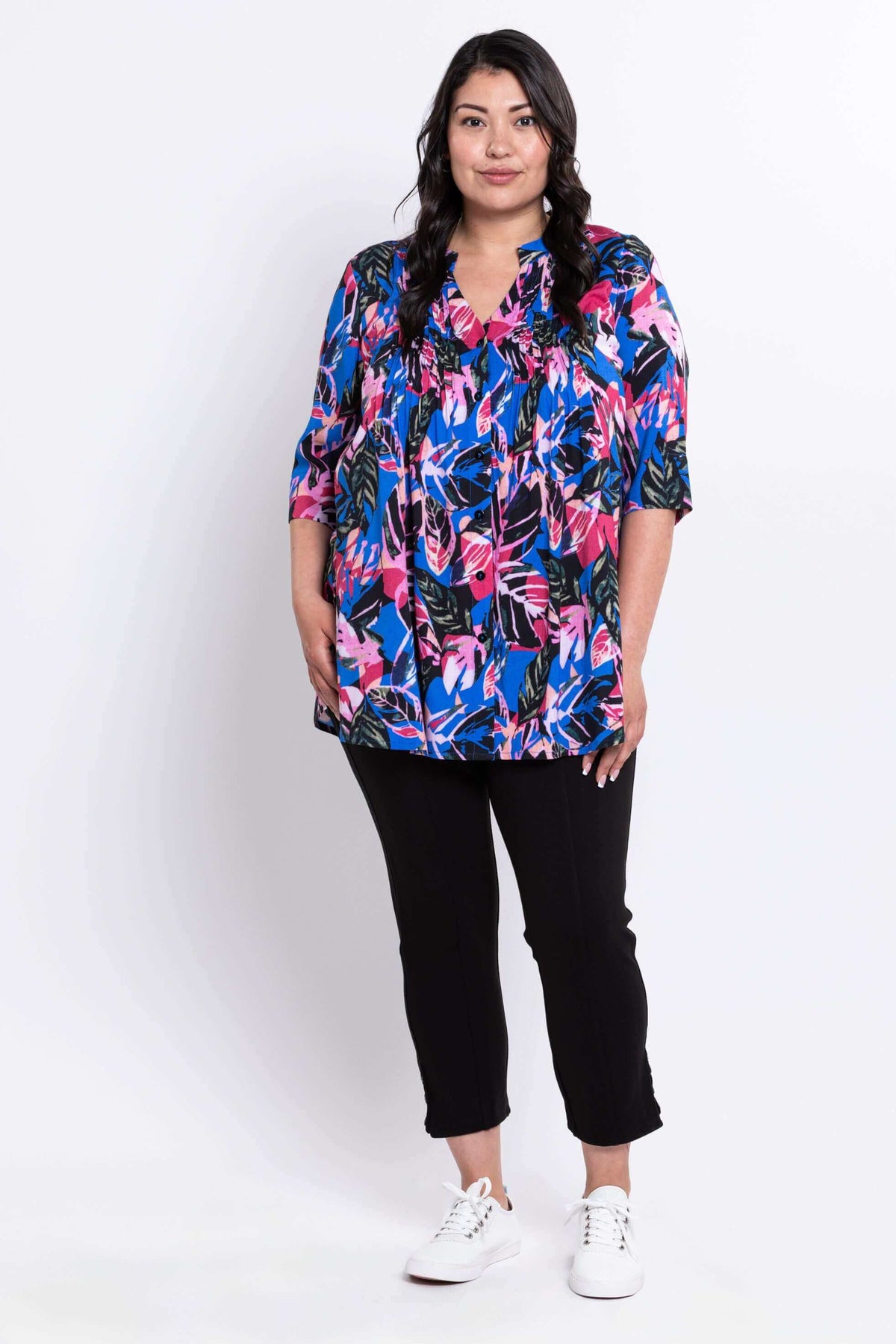Full body front view of woman modeling bright botanical print blouse and black slim fit pants