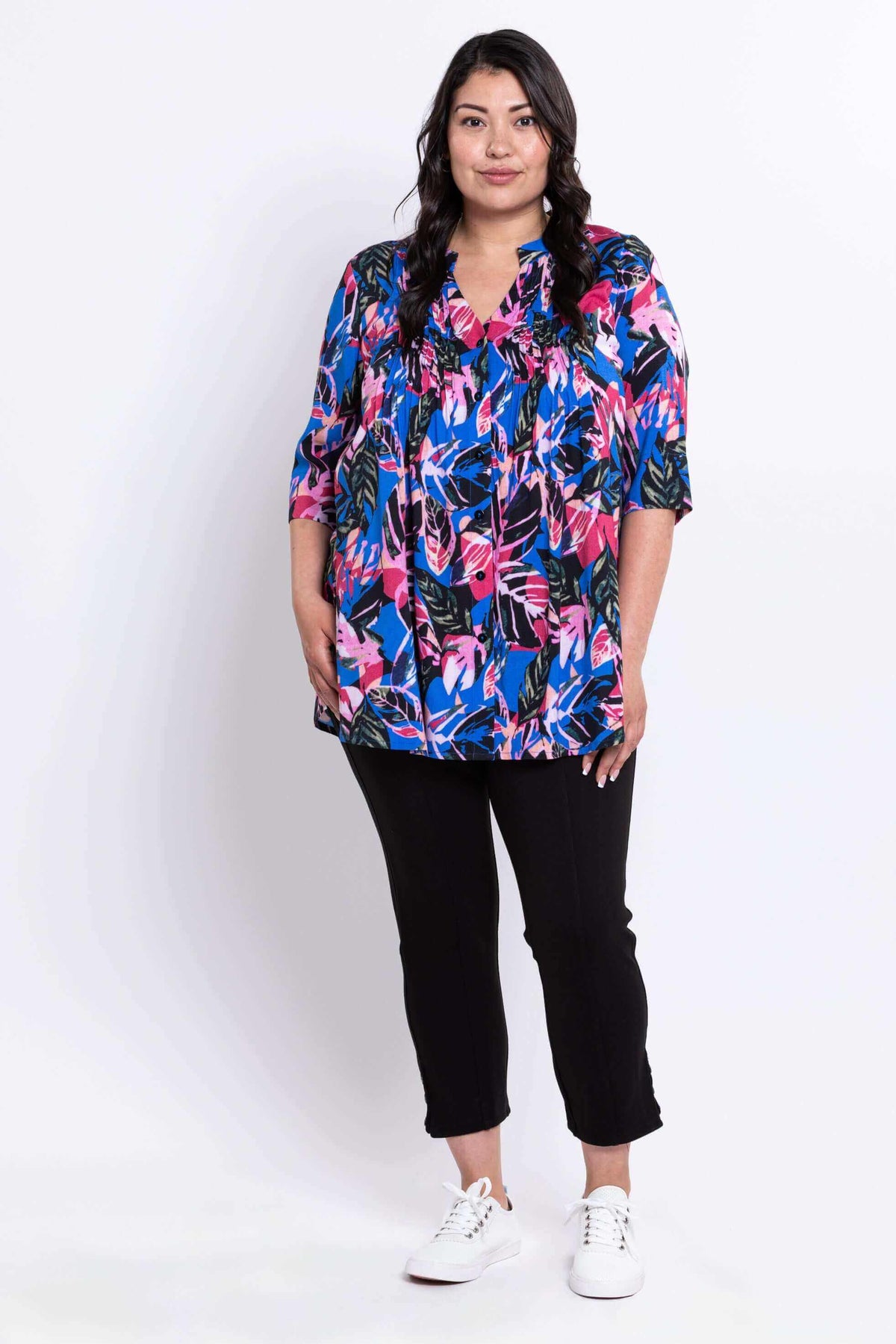Full body front view of woman in a Margate blouse with bright leaf print and black pants