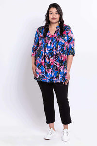 Full body front view of woman in a Margate blouse with bright leaf print and black pants