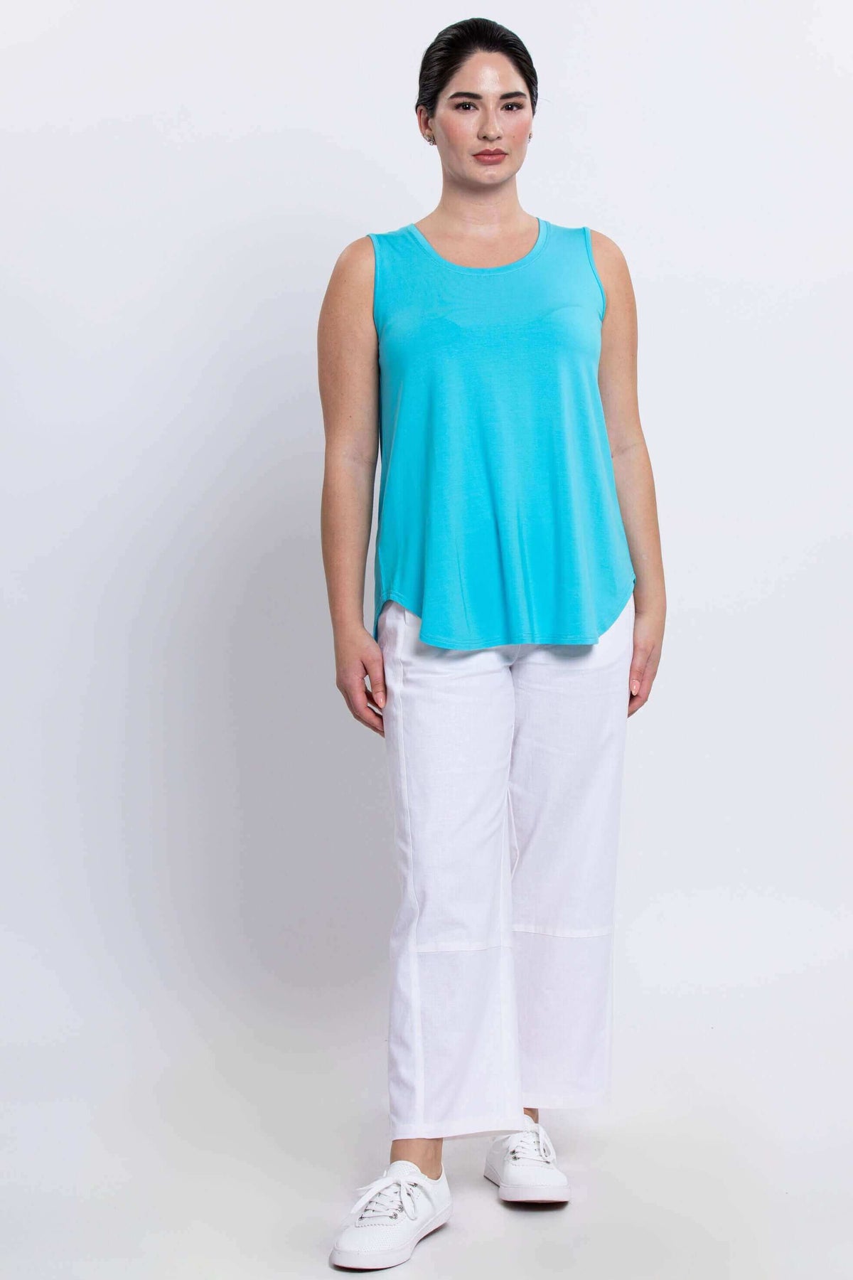 Full front body view of a woman wearing an aqua sleeveless tank and white pants