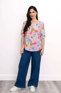 Full body front view of model in floral blouse and blue pants with white sneakers