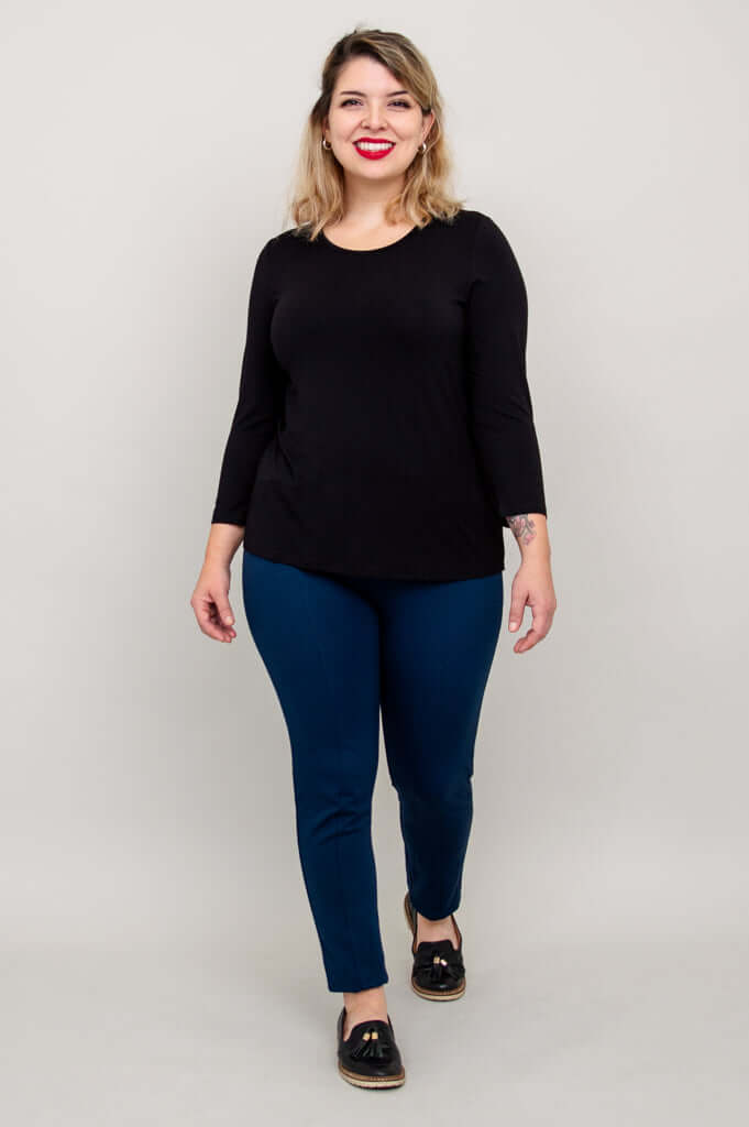 Model smiling in a black 3/4 sleeve tee and blue pants, full body front view