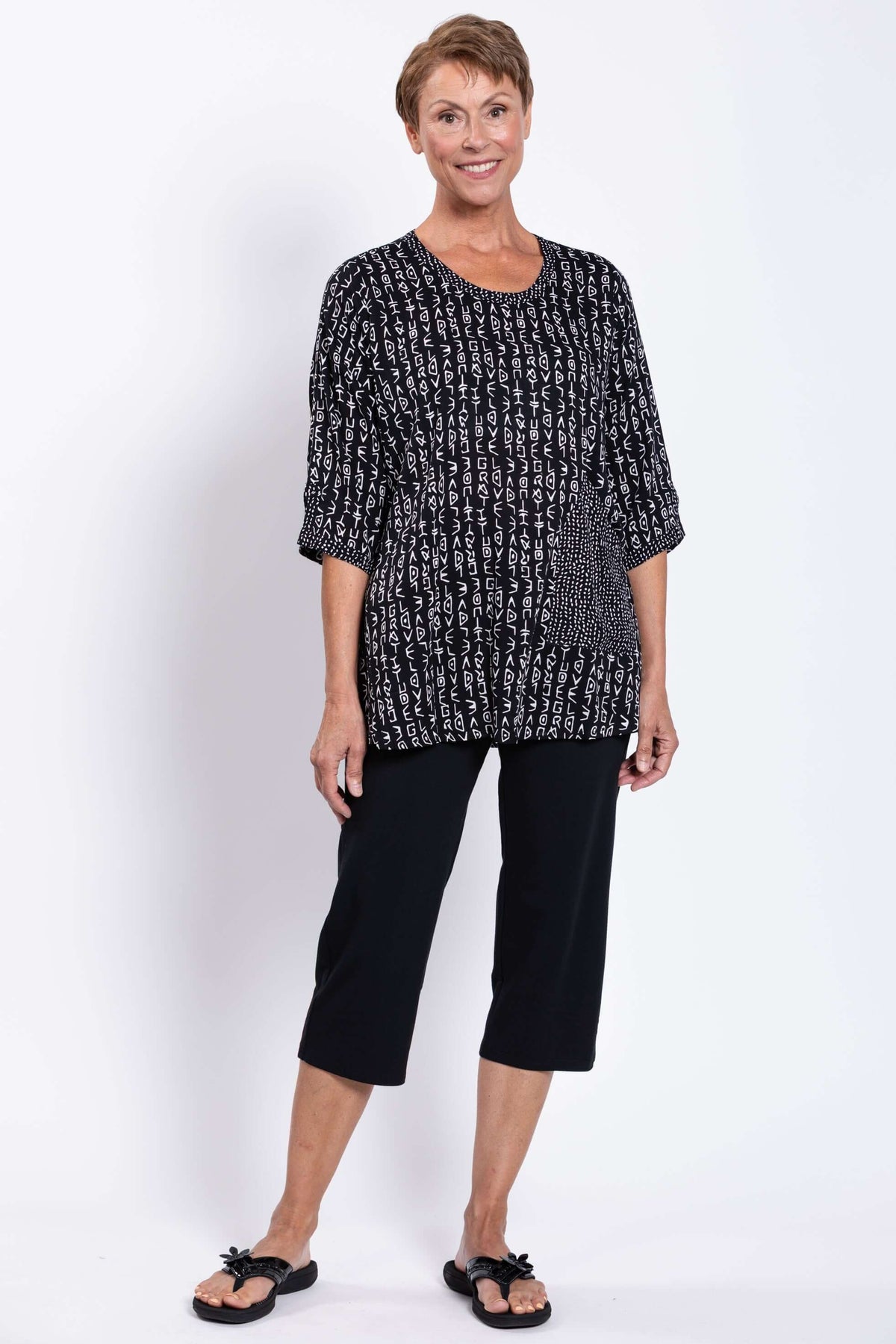Full body front view of a woman modeling a black and white patterned blouse and black pants