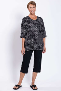 Full body front view of a woman modeling a black and white patterned blouse and black pants