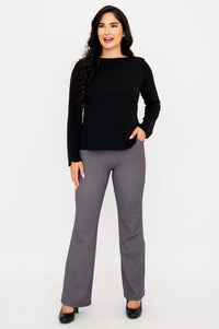 Woman wearing a black long sleeve boat neck top and gray check pants, standing full length