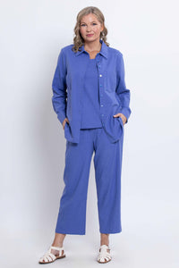 Woman standing in a blue shirt and pants set, hands in pockets, full body front view