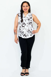 Full body view of woman in sleeveless black and white floral shirt with black pants and sandals