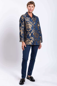 Full body front view of woman styled in blue and gold ornate jacquard coat and navy pants
