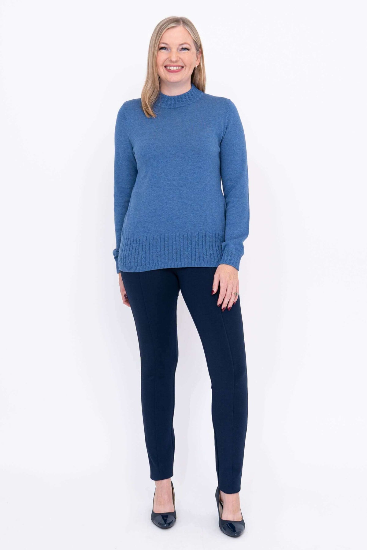 Full body front view of woman in blue cable knit sweater and navy trousers