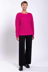 Full body front view of a woman modeling a fuchsia sweater with black pants