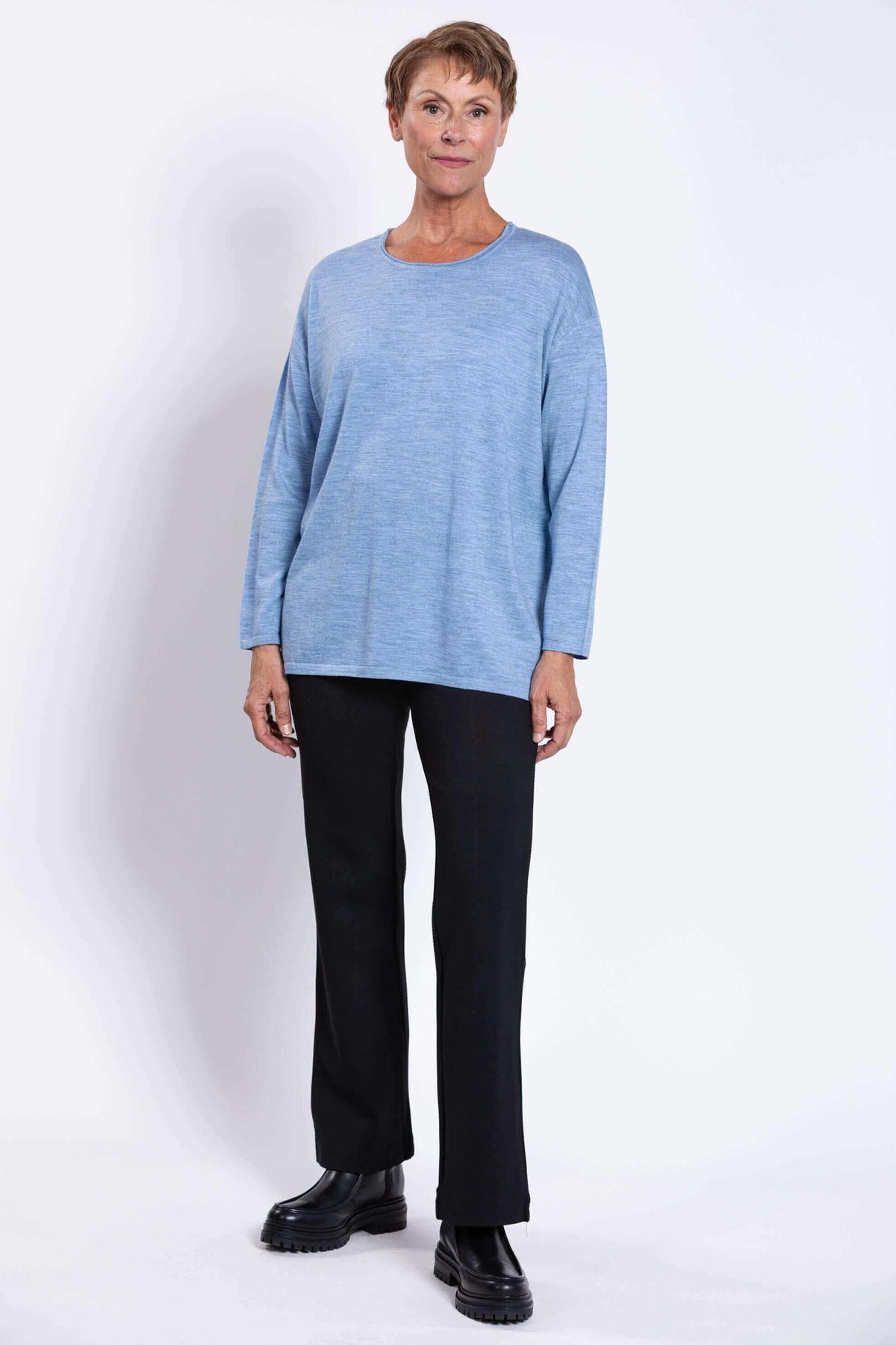 Full body front view of woman in light blue Merino sweater and black pants with boots