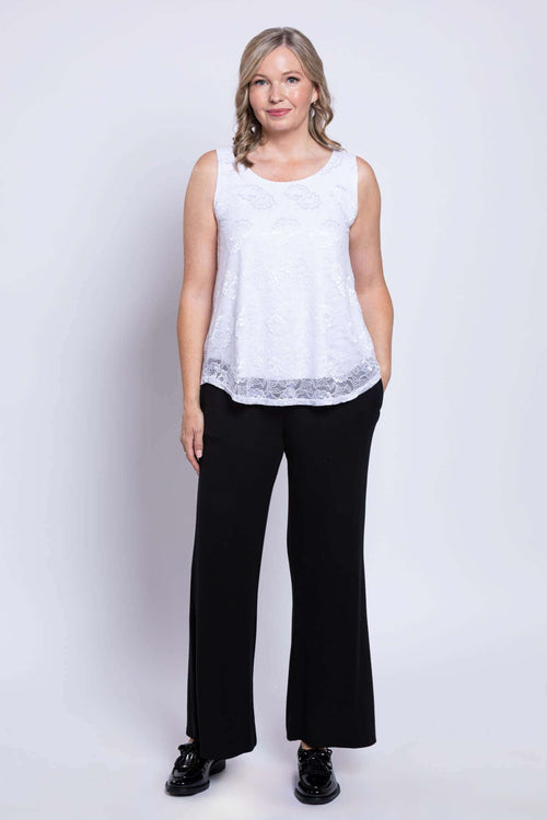 Full body front view of woman in white lace tank top and black pants