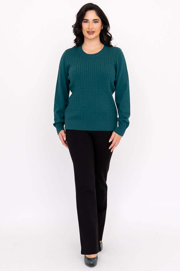 Full body front view of a woman in a teal crew neck cable knit sweater and black pants