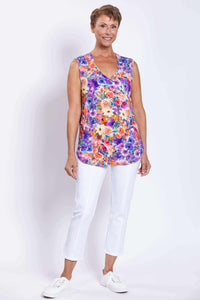 Full body view of a woman in a vibrant floral sleeveless top and white pants