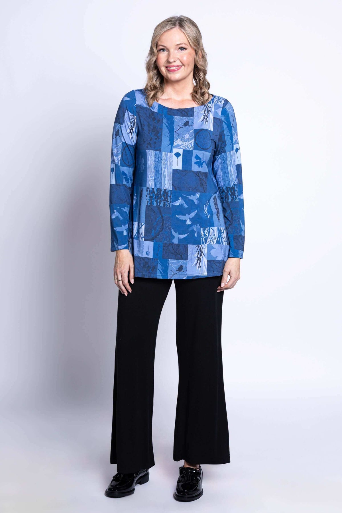 Full body image of model in blue patchwork tunic and black pants