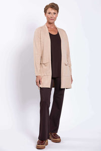 Full body view of a woman in a beige cardigan, dark brown top and pants with brown shoes