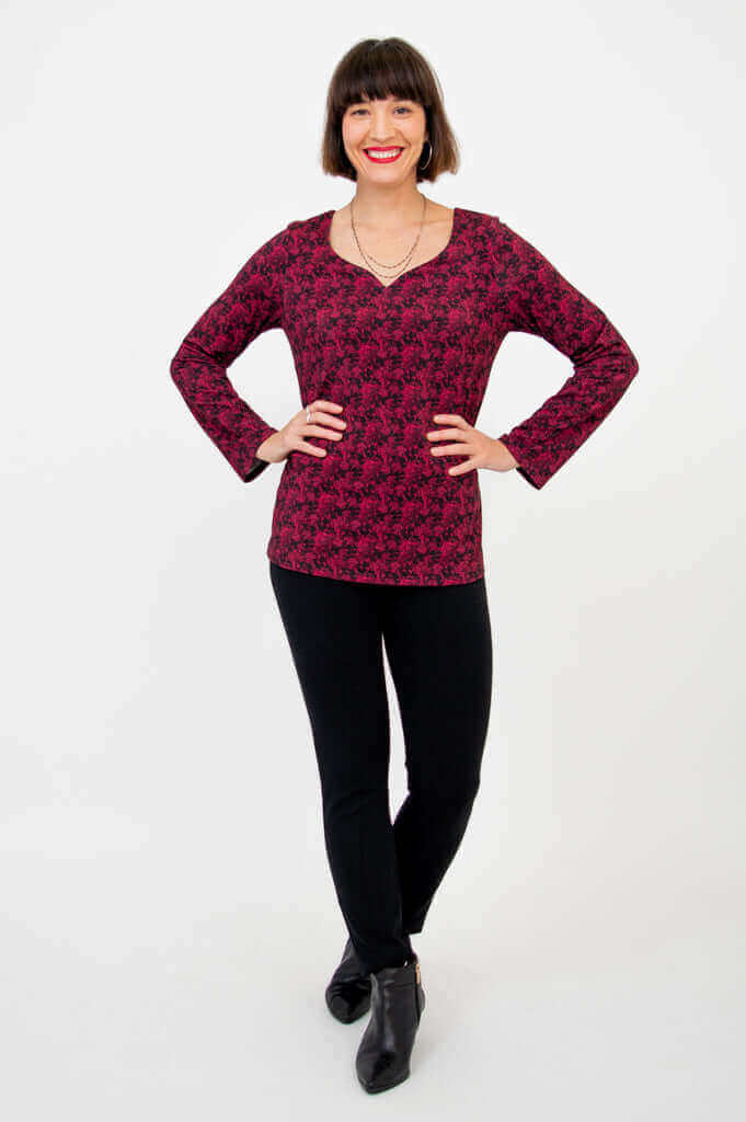 Full body view of woman in maroon floral sweetheart top and black pants, hands on hips
