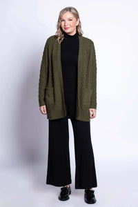 Full body view of a woman in an olive green cable knit cardigan and black pants