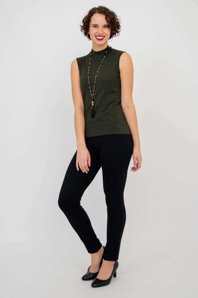 Woman standing in sleeveless olive-green mock neck sweater and black slim pants, full body