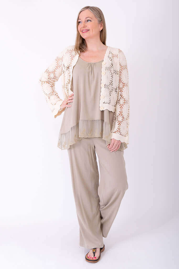 Full body shot of woman modeling a cream crochet cardigan, wide-leg pants, and sandals