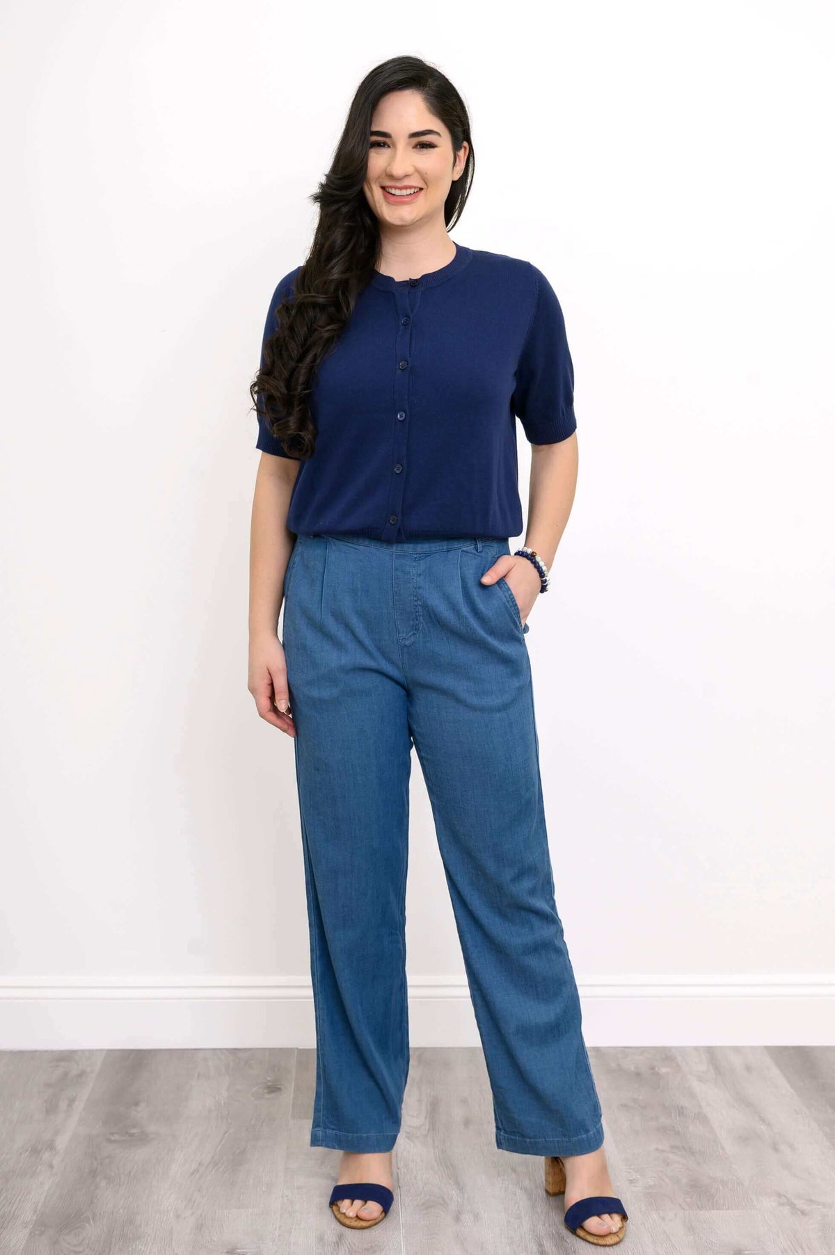 Full body view of model in navy short sleeve Shen cardigan and blue pants with hands in pockets