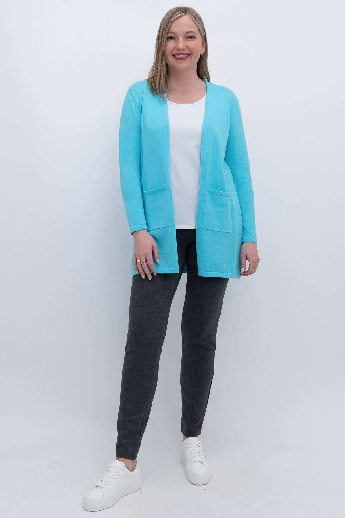 Full body view of woman in aqua blue open cardigan, white top, and dark pants