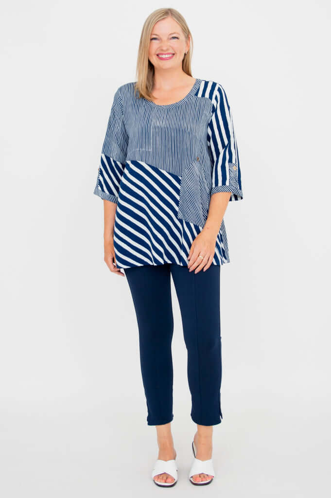 Full body view of woman in navy and white striped blouse and navy pants, standing and smiling