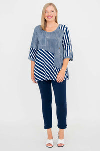 Full body view of woman in navy and white striped blouse and navy pants, standing and smiling